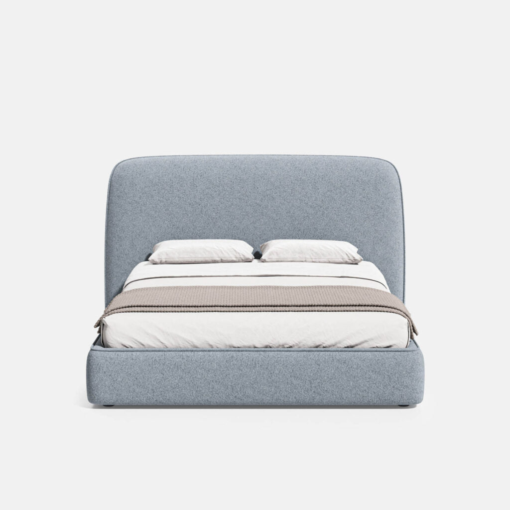 A modern platform bed with a tall, rounded headboard and matching upholstered base, shown in a light gray fabric. The bed is styled with white bedding, two white pillows, and a beige striped throw blanket, set against a plain white background.