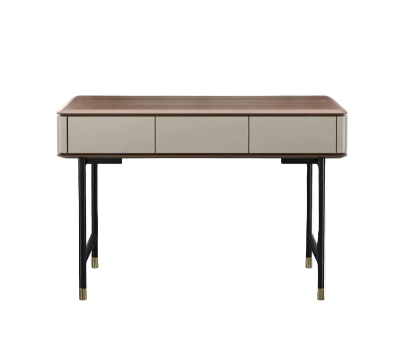 A modern writing desk with a medium brown wood top, three light beige drawers, and black metal legs with gold-toned caps, shown against a plain white background.