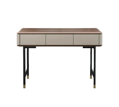 A modern writing desk with a medium brown wood top, three light beige drawers, and black metal legs with gold-toned caps, shown against a plain white background.