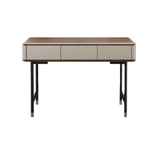 A modern writing desk with a medium brown wood top, three light beige drawers, and black metal legs with gold-toned caps, shown against a plain white background.